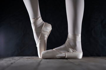 detail of female ballet dancer's feet in ballet position with pointe shoe in front of dark background 