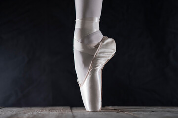 detail of female ballet dancer's foot in ballet position with pointe shoe in front of dark...