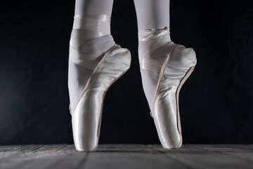detail of female ballet dancer's feet in ballet position with pointe shoe in front of dark...