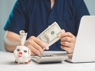 A piggy bank with a $100 bill with a background of a man holding US dollar bills while sitting at a desk
