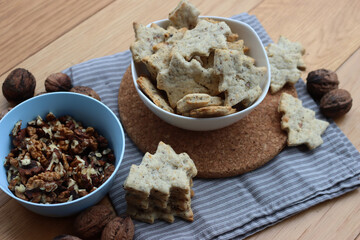 Walnut cookies in shape of a tree ina white bowl with dry walnuts on woooden table 