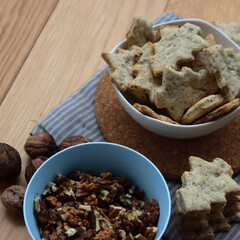 Walnut cookies in shape of a tree ina white bowl with dry walnuts on woooden table 