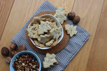 Top view of Walnut cookies in shape of a tree in a white bowl with dry walnuts on woooden table 