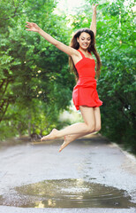 Young happy woman wearing red dress jumping into a puddle