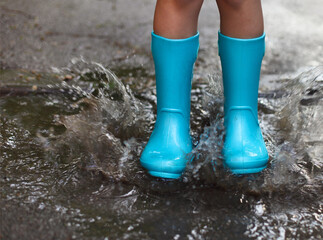 Child wearing blue rain boots jumping into a puddle
