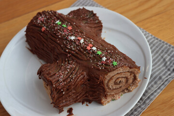 Close-up of a chocolate yule log filled with chestnut cream on a plate on  wooden table. Traditional festive Buche de Noel