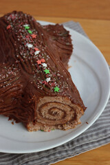 Close-up of a chocolate yule log filled with chestnut cream on a plate on  wooden table. Traditional festive Buche de Noel