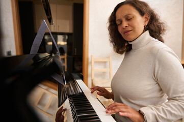 Young adult multi ethnic woman learning basic of classic piano at home. Practicing chord instrument.