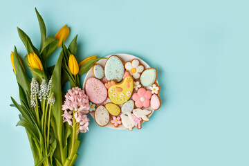 Easter gingerbread with icing on plate, seasonal flowers on blue, festive Easter background web banner, copy space. Easter card with traditional treats. Sweet Easter concept, greeting card