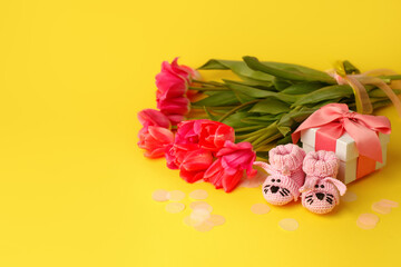 Pair of small pink baby socks, tulips and gift box on yellow background with gift present boxes and copy space for your warm message, baby shower, first newborn party background, banner