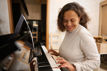 Happy African American young adult woman smiling while playing grand piano, practicing the chord...