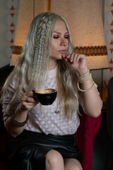 Platinum blonde girl, 25-30 years old, wearing a pink sweater, sitting with a black cup of hot coffee. In a 70s style restaurant.
