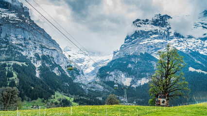 The Swiss Alps with a dreamy landscape with majestic peaks under clouds. Cable cars operate between...