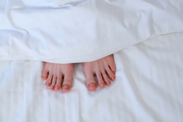Woman's feet fingers in bed look out the white linen, she sleeping alone. Healthy sleep relaxation,...