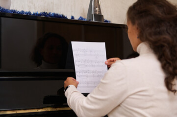 Rear view of a pianist holding notes of classic musical composition, sitting at black old piano,...