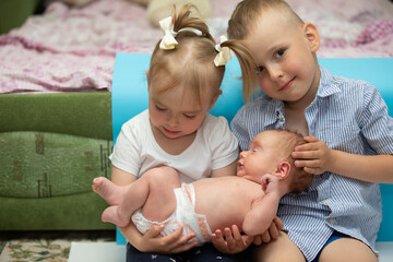 Little brother and sister rejoice at the newborn baby. Three children of different ages in a home...