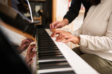 Female hands playing grand piano under the guidance of music teacher. Close-up fingers touch ebony and ivory piano keys
