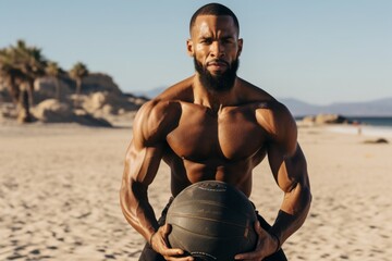 Young shirtless African man exercising with medicine ball during his outdoor workout on the beach