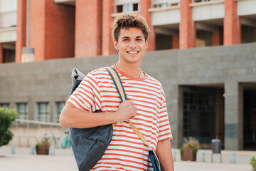 Close up individual portrait of a handsome student young man standing at university campus. Happy teenage male smiling and looking at camera. Proud high school guy staring front carrying a backpack