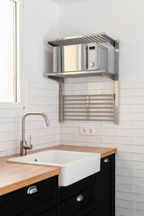 View of a white modern kitchen sink with dark countertops and cabinets and rails and white tiles on window background. The concept of a modern kitchen in a new building