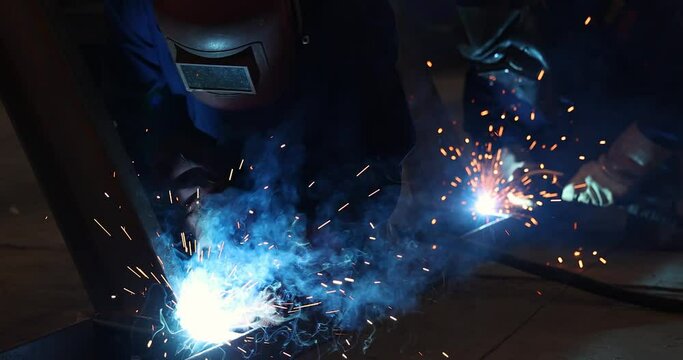Welders at work in metal industry, welding metal construction - slow motion. Close-up - zoom in shot lots of sparks in the factory