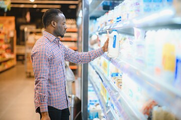 Portrait of smiling man at supermarket. Young african man with shopping basket in grocery store