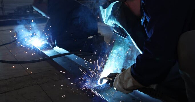 Welders at work in metal industry, welding metal construction - slow motion. Close-up shot lots of sparks in the factory