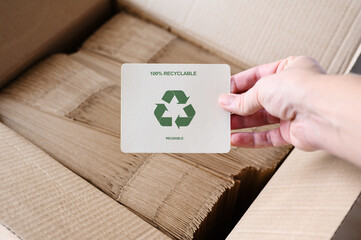 A sign with a recycling sign in a hand against the background of a box with paper bags. Production...
