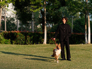 Naklejka na ściany i meble Portrait of a handsome Chinese young man in black with his rough collie dog on green grass field in sunny day, male fashion, cool Asian young man lifestyle, harmony man and pet.