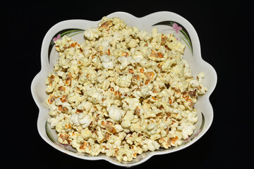 Delicious popcorn lies in a plate on a dark background.