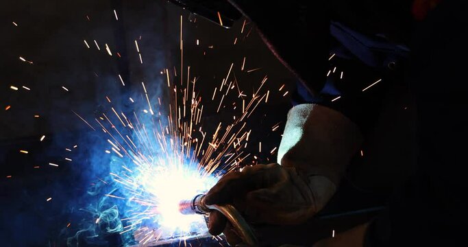 Welder at work in metal industry, welding metal construction - slow motion. Close-up shot lots of sparks in the factory