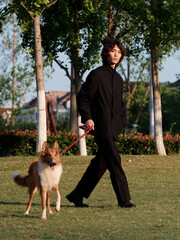 Portrait of a handsome Chinese young man in black with his rough collie dog on green grass field in sunny day, male fashion, cool Asian young man lifestyle, harmony man and pet.