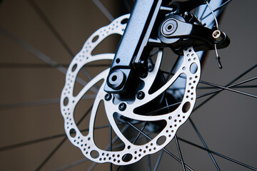 Part of the bicycle's braking system. Grey metal brake disc and brake pads on road bike, close up.