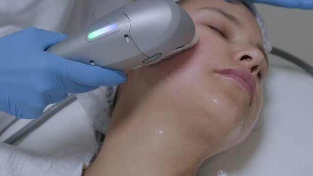 Hardware ultrasound cosmetic procedure in a beauty clinic. Skin rejuvenation, smas lifting anti-age therapy. Close-up beautician hands work with female patient face skin.