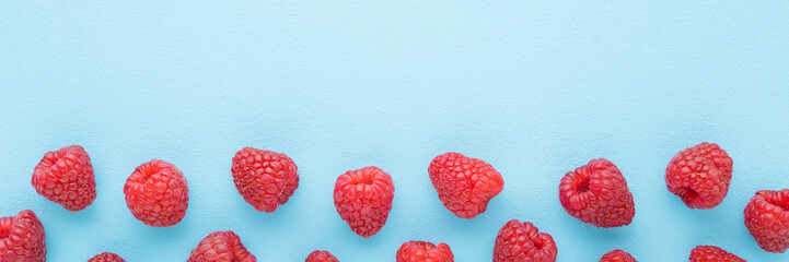 Fresh red raspberries on light blue table background. Pastel color. Wide banner. Closeup. Top down...