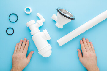 Young adult man hands assembling white new plastic parts for sink drain siphon. Light blue table...
