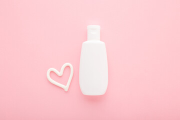 Heart shape created from cream. White plastic bottle on light pink table background. Pastel color....