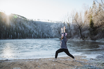 The girl is doing yoga on the smell of the rising sun in the mountains, training in the fresh air, sporing classes on the shore of the lake, winter training.