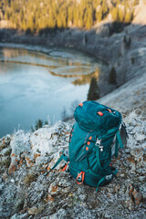 A tourist backpack stands on a stone against the background of a mountain lake, camping equipment, a bag for things.