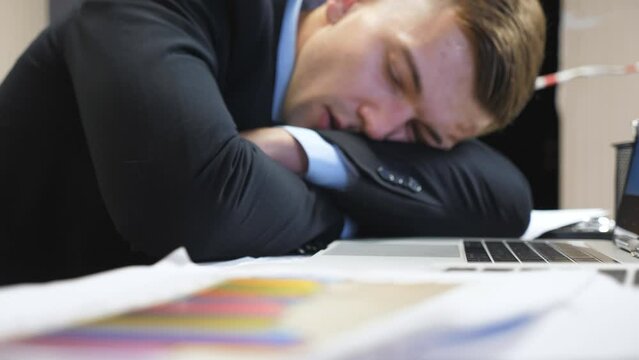 Dolly shot to tired boss in formal suit falling asleep on table at boardroom. Exhausted manager sleeping on table with laptops at office. Young entrepreneur napping at workplace. Close up Slow motion