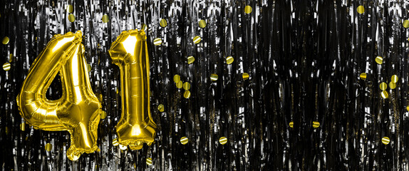 Gold foil balloon number number 41 on a background of black tinsel decoration. Birthday card,...