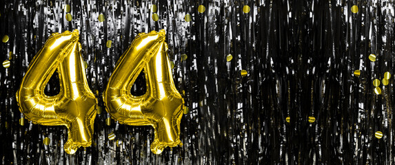 Gold foil balloon number number 44 on a background of black tinsel decoration. Birthday card,...