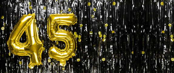 Gold foil balloon number number 45 on a background of black tinsel decoration. Birthday card,...