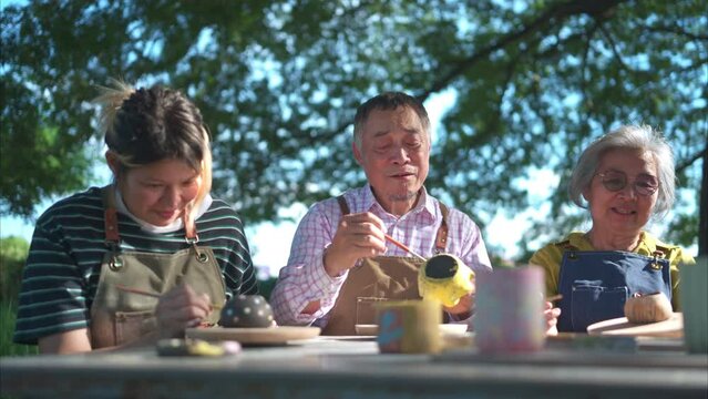 In the pottery workshop, an Asian retired couple is engaged in pottery making and clay painting activities.