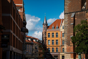 Blick in eine Altstadt mit historischen Hausfassaden und Kirchturm vor blauem Himmel