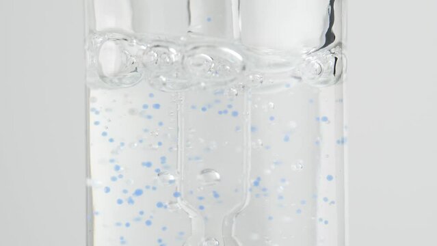 Drop is combined with a cosmetic serum. Serum with blue granules. A bubble of air in a jar. Macro. Slow motion.
