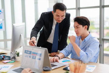 two Asian businessperson colleagues discussing with computer in office.