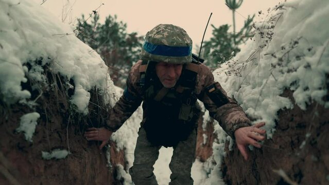 An armed Ukrainian soldier sneaks crouched in a trench during hostilities. Ukraine's war with Russia.