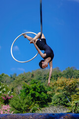Beautiful Asian girl performing show aerial hoop or aerial ring in various positions and spinning stunts on the blue sky around the natural fresh and the waterfall, outdoors. © pomphotothailand