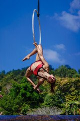 Beautiful Asian girl performing show aerial hoop or aerial ring in various positions and spinning stunts on the blue sky around the natural fresh and the waterfall, outdoors.